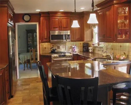 Warm wooden kitchen with granite island, pendant lights, and stainless steel appliances In Bucks County PA