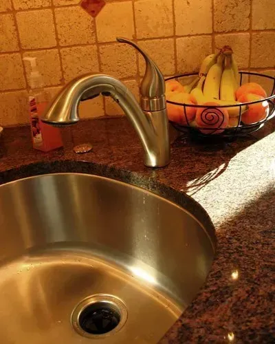 Kitchen sink and faucet on a granite countertop, with a bowl of bananas in the background In Bucks County PA