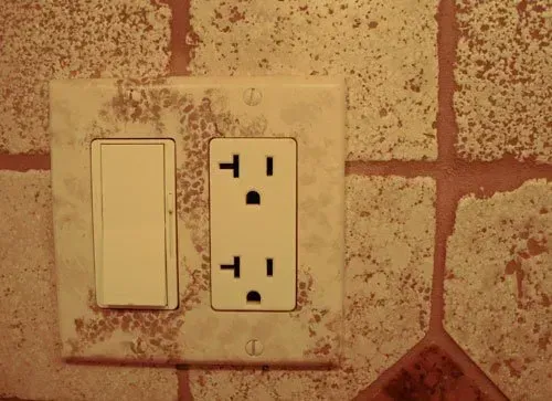 Light switch and electrical outlet on a beige wall with red tile backdrop In Bucks County PA