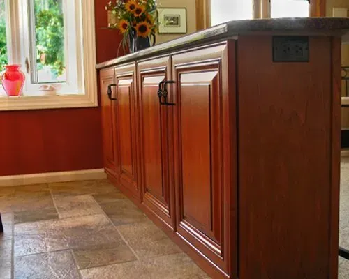 Wooden kitchen island with dark countertop in a red-walled room by a sunlit window In Bucks County PA