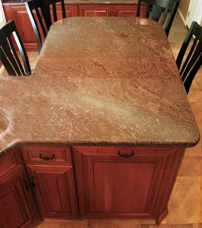 Brown stone kitchen island countertop viewed from above, with wood cabinetry and black barstools around it In Bucks County PA