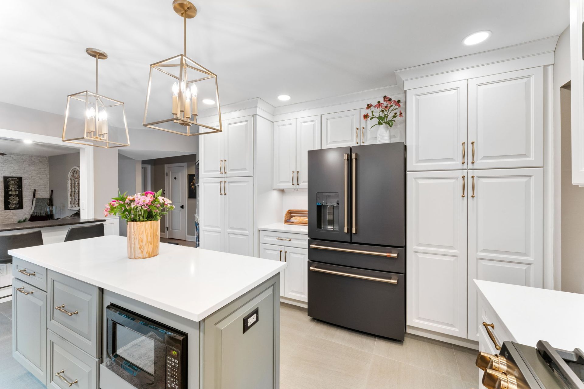Bright white kitchen with gold pendant lights, black refrigerator, and large center island In Bucks Country PA