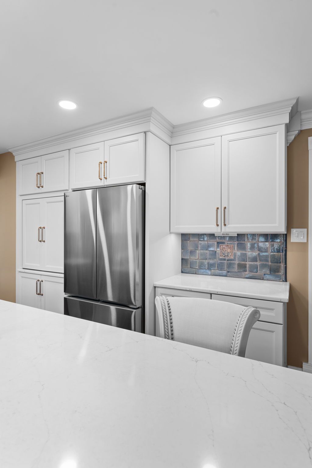 Modern white kitchen with stainless steel fridge, built-in cabinets, and marble island counter  In Bucks County PA
