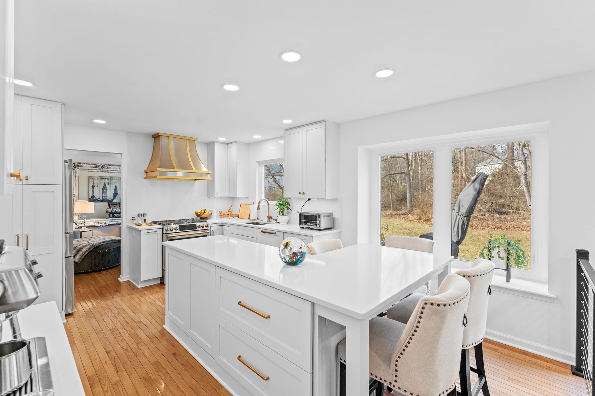 Bright white kitchen with island, wood floors, and large windows overlooking trees In Bucks Country PA