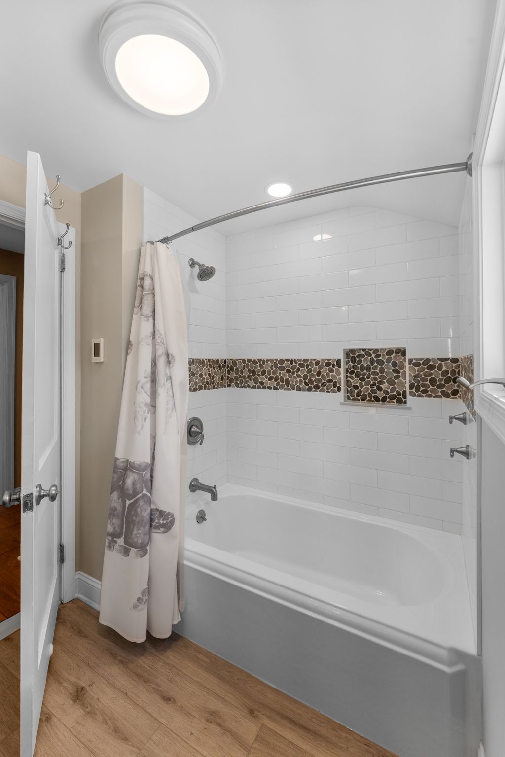 Small bathroom with white tub, tiled shower, gray curtain, and wood-look floor  In Bucks County PA