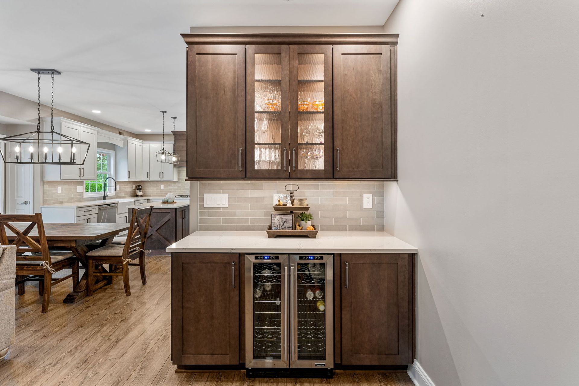 Kitchen wet bar with dark wood cabinets, white countertop, and glass-front wine fridge in a bright dining area  In Bucks County PA