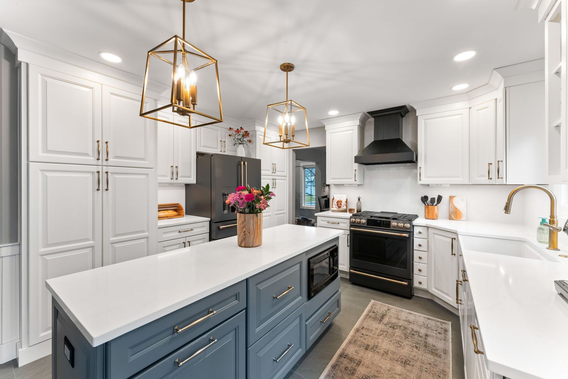 Bright white kitchen with blue island, black stove, and gold pendant lights In Bucks Country PA