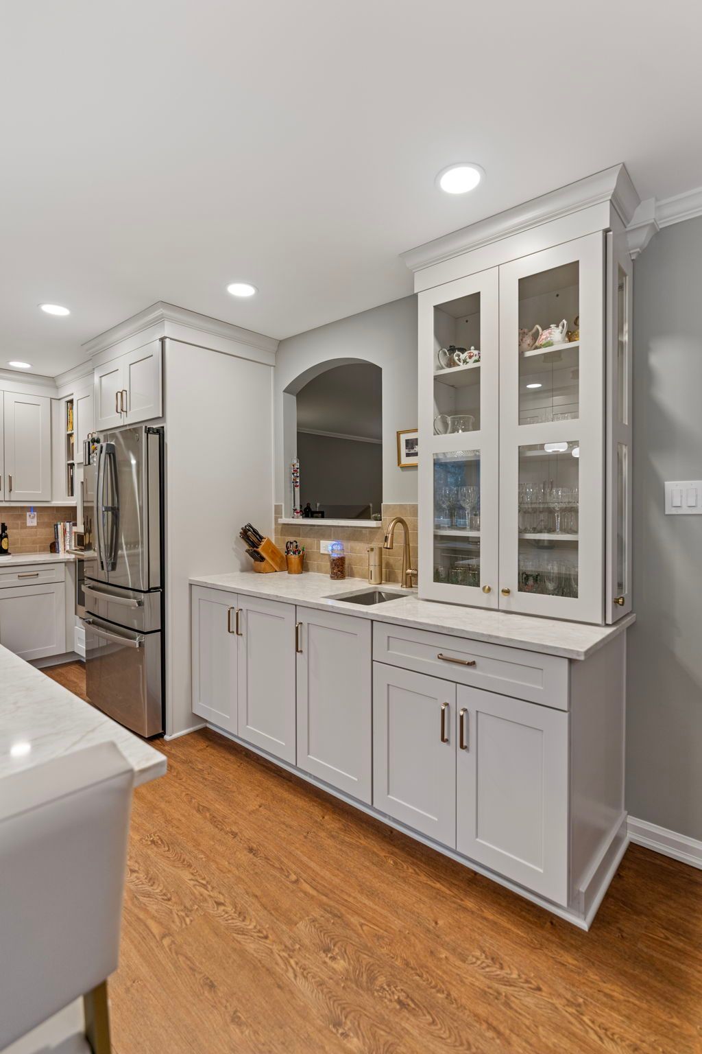 Bright white kitchen with glass-front cabinets, stainless fridge, and wood floors In Bucks County PA