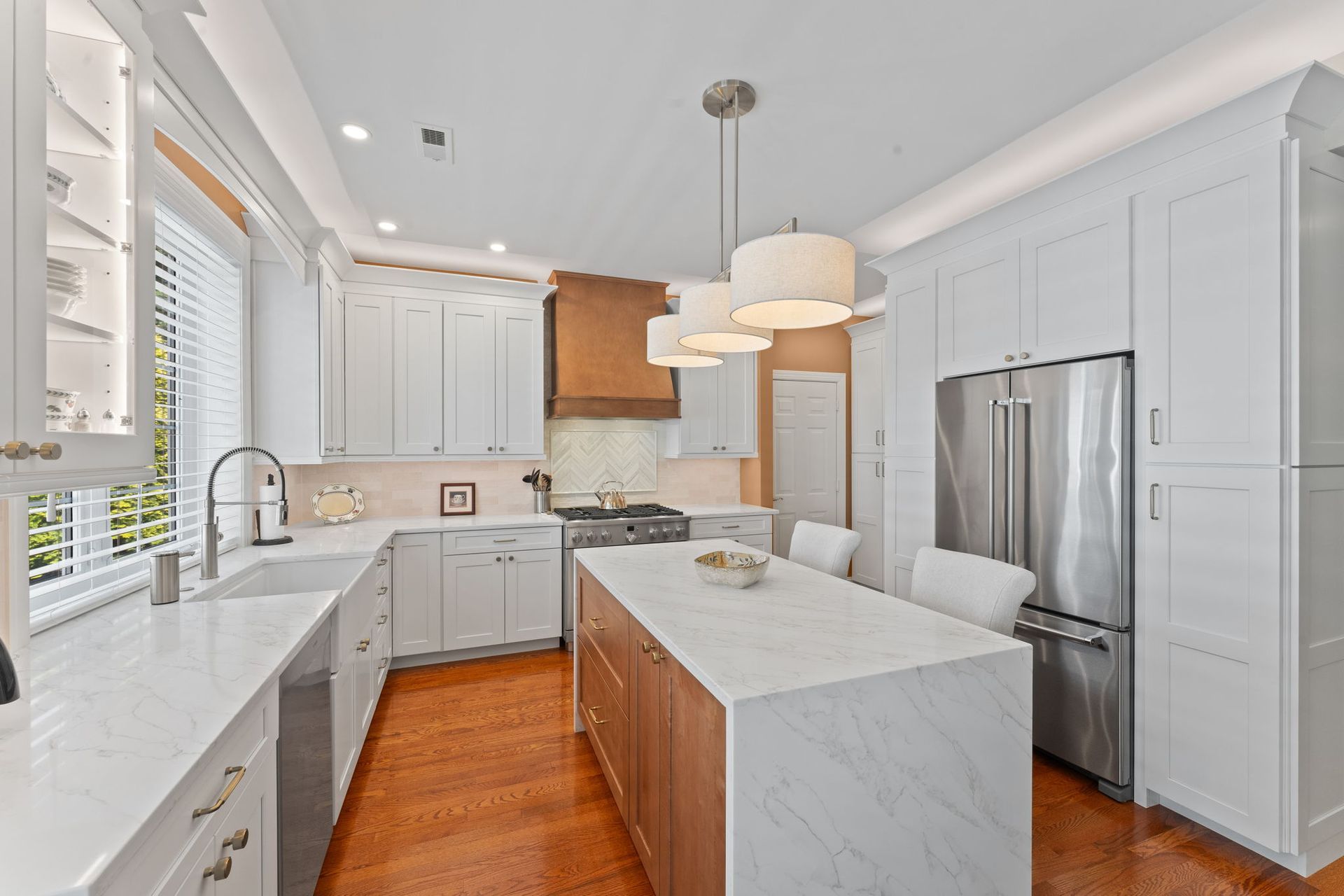 Bright white kitchen with marble island, stainless fridge, pendant lights, and hardwood floors In Bucks County PA