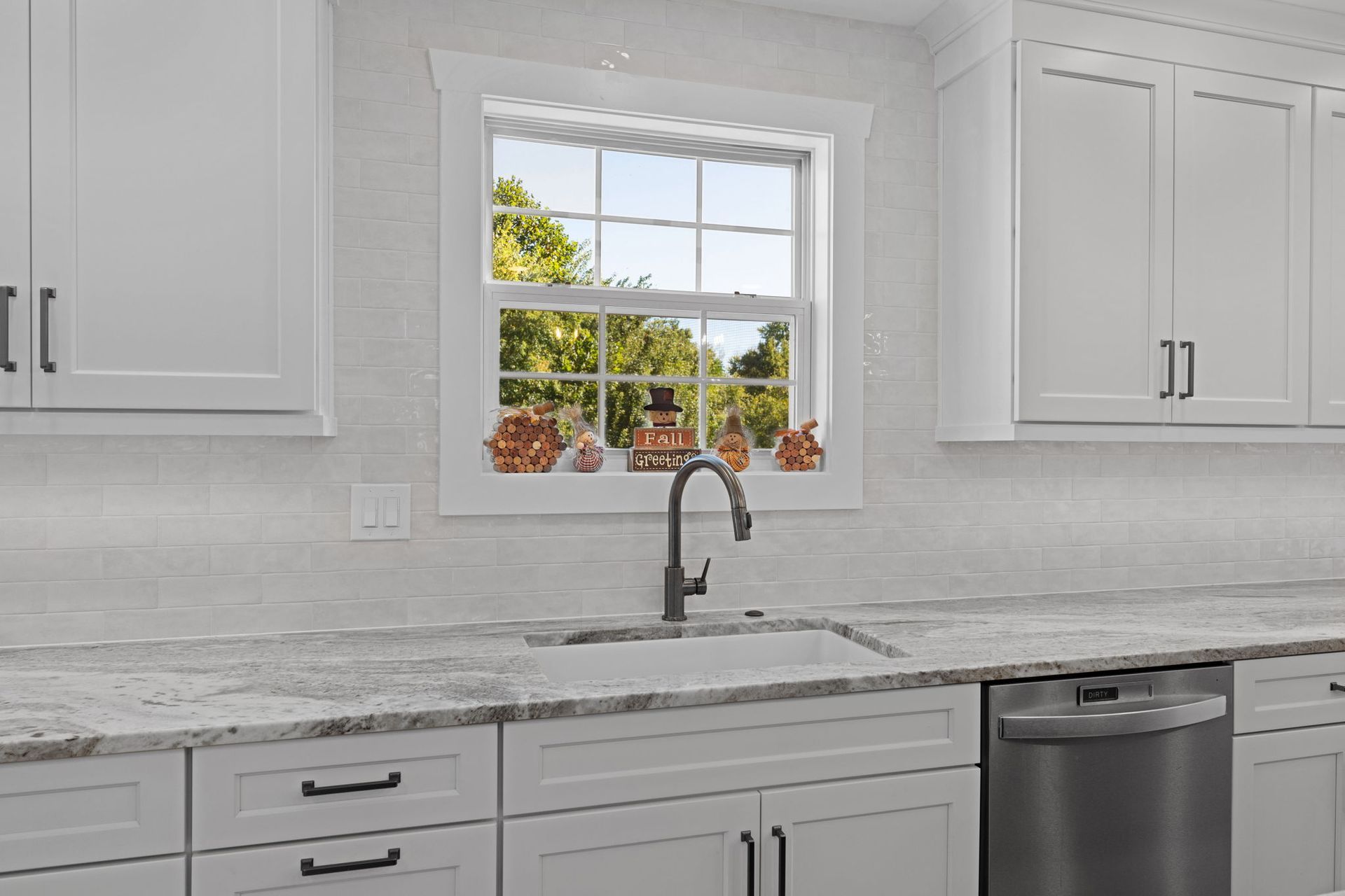 Bright white kitchen with a window over a sink and gray countertops, plus a stainless dishwasher In Bucks County PA
