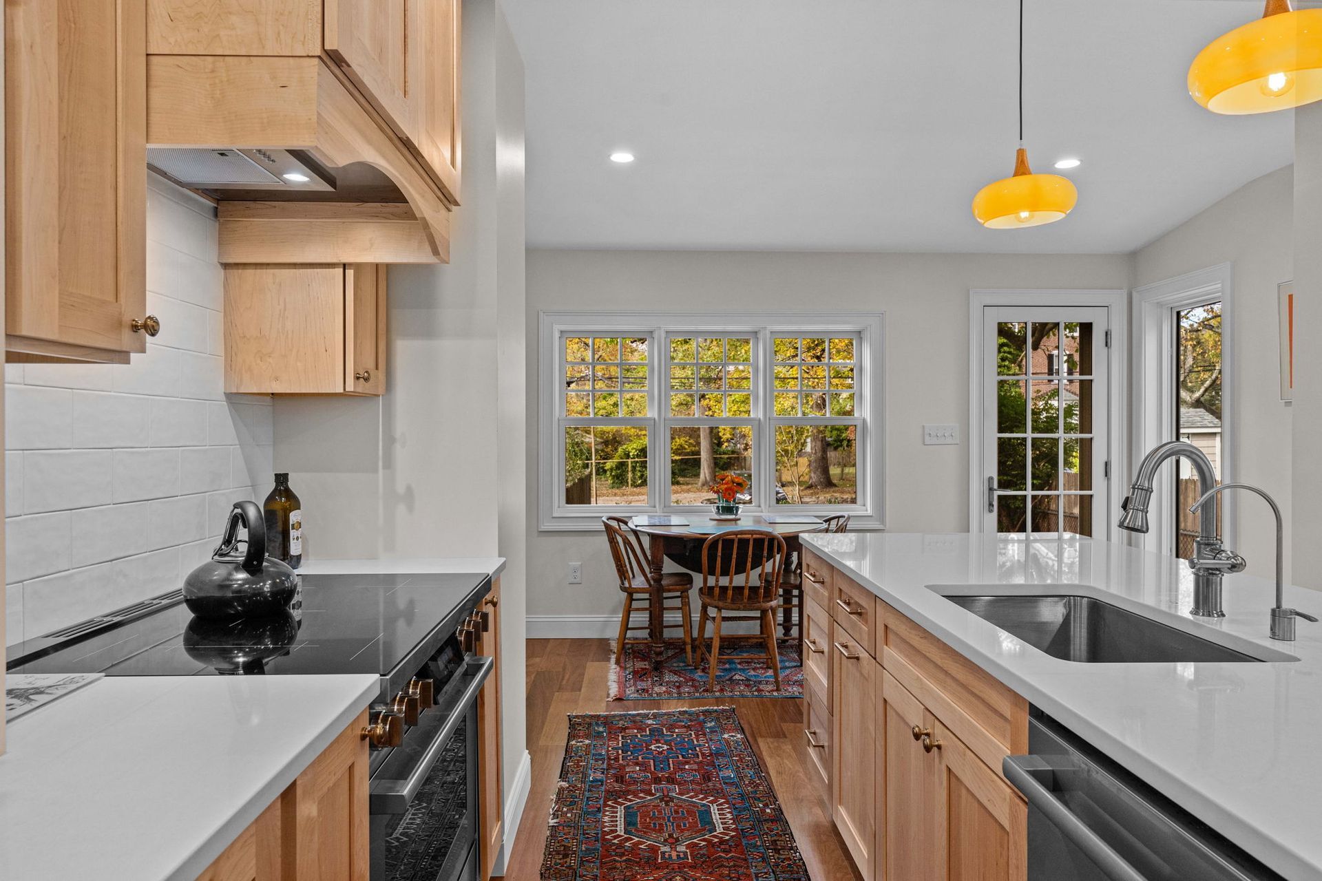 Bright modern kitchen with wood cabinets, white counters, and a dining nook by autumn-colored windows In Bucks County PA