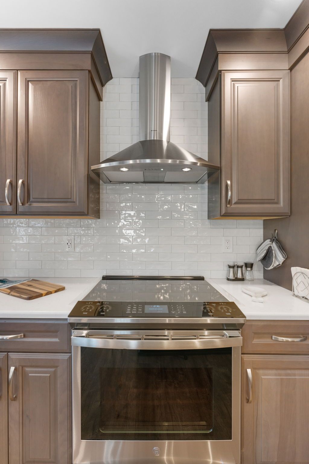 Modern kitchen with stainless steel stove and hood, white backsplash, and dark wood cabinets In Bucks Country PA