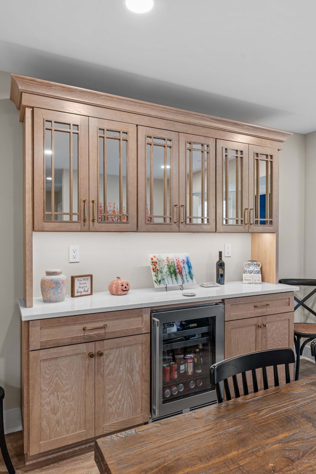 Wooden home bar cabinet with glass-front upper cabinets, countertop decor, and built-in wine fridge against a wall in Bucks County PA