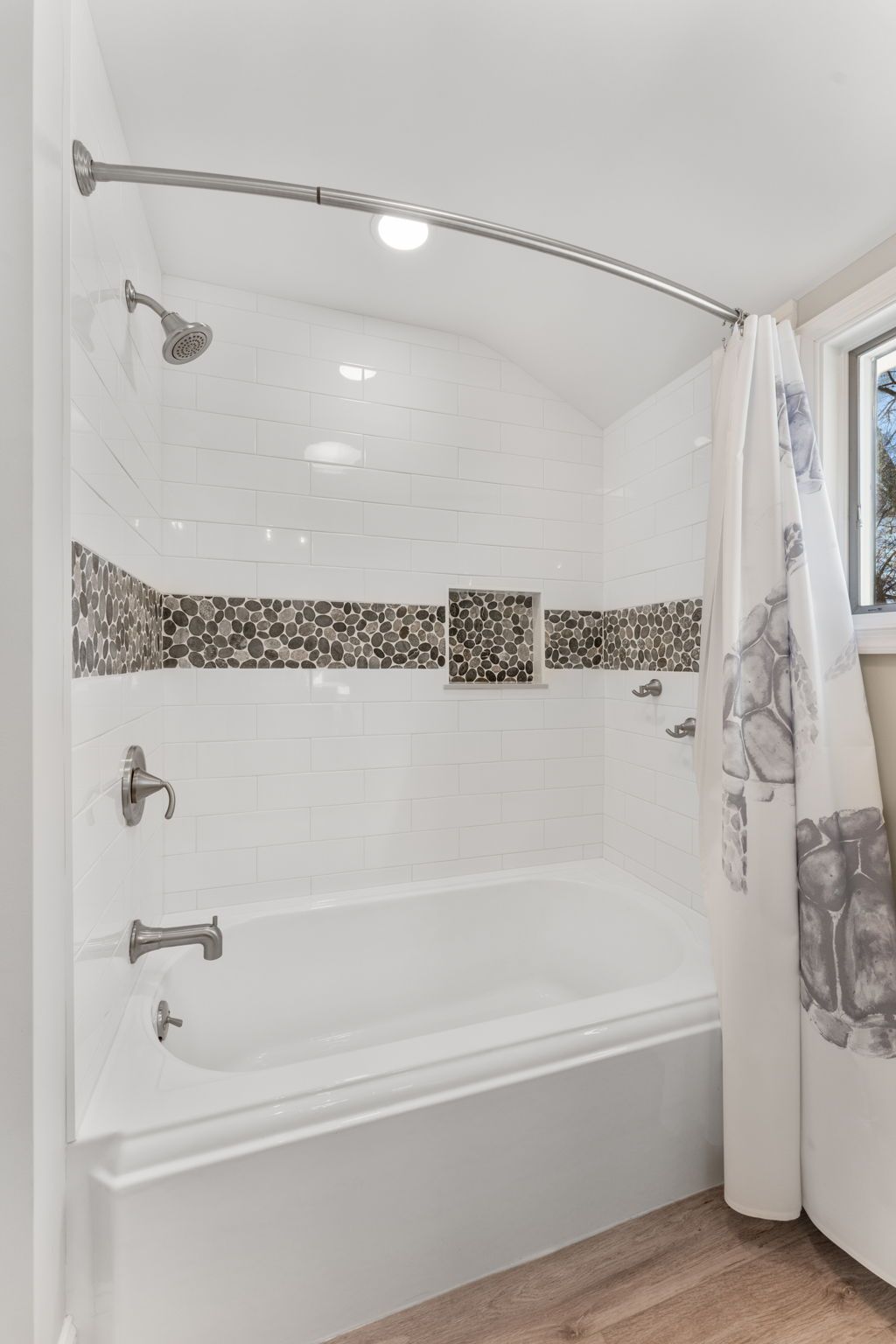 White tiled bathroom with a bathtub, curved shower rod, and mosaic accent border In Bucks County PA
