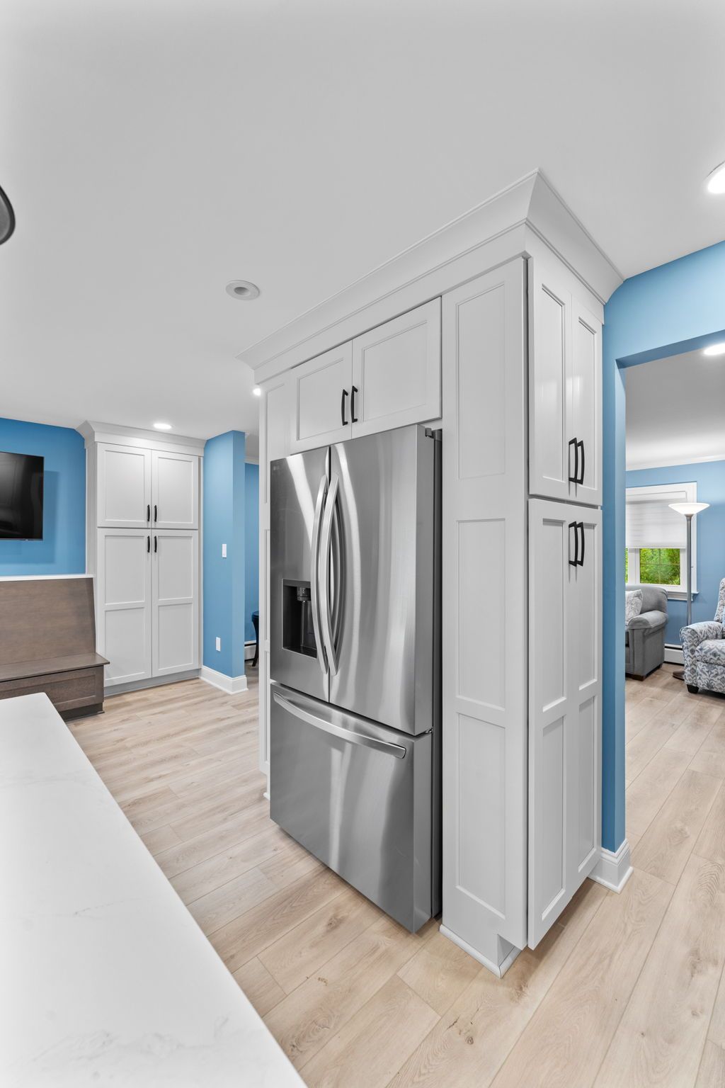 Modern kitchen with stainless steel refrigerator, white cabinets, and light wood floors in Bucks County PA