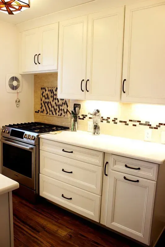 Compact kitchen with white cabinets, dark wood floor, mosaic backsplash, stove, and under-cabinet lighting In Bucks Country PA