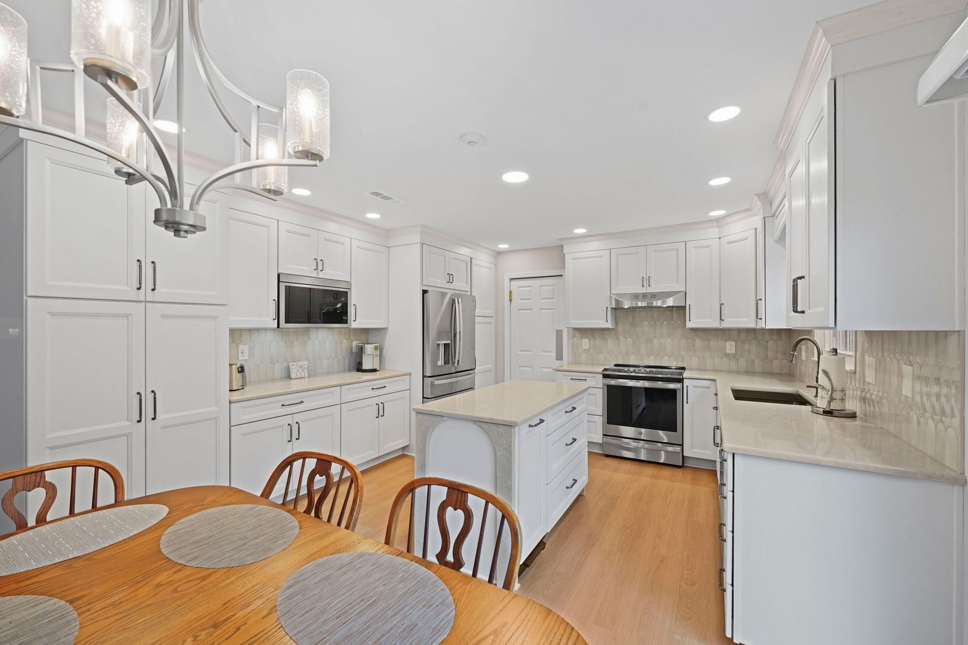 Bright white kitchen with island, wooden dining table, and stainless appliances under pendant lights in Bucks County PA
