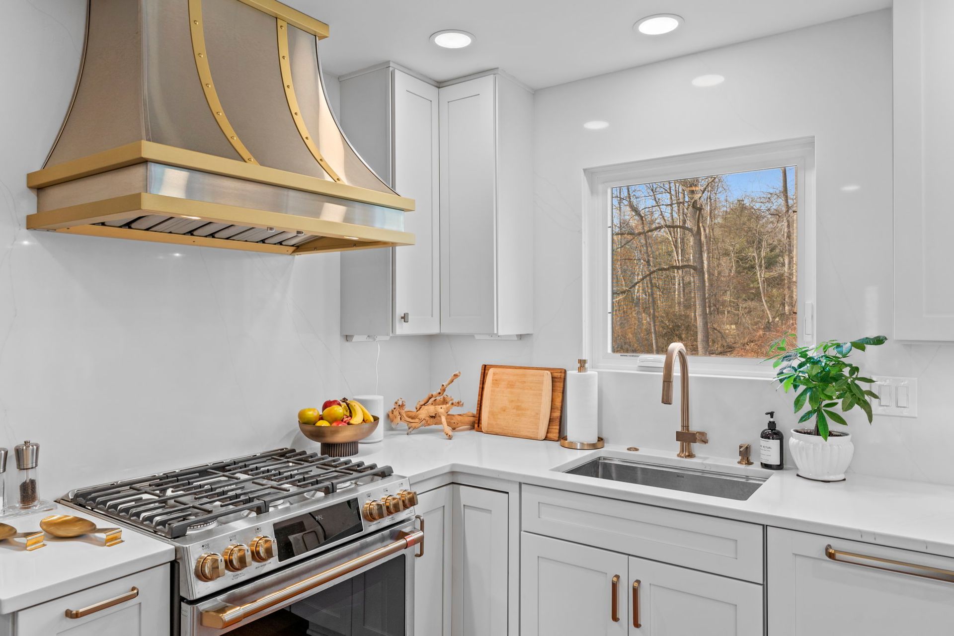 Bright white kitchen with stainless range hood, gas stove, sink, and window view of trees In Bucks Country PA