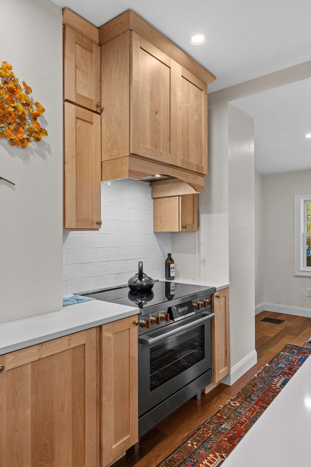Narrow kitchen with light wood cabinets, stainless stove, white tile backsplash, and patterned runner rug In Bucks County PA