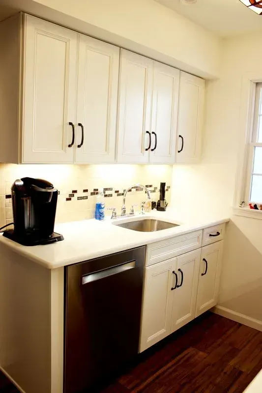 Compact white kitchen with upper cabinets, coffee maker, sink, and dark wood floor In Bucks County PA