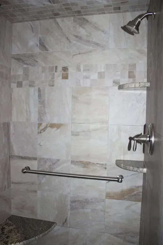 Bathroom shower with tiled walls, glass shelf, grab bar, showerhead, and built-in bench seat  In Bucks County PA