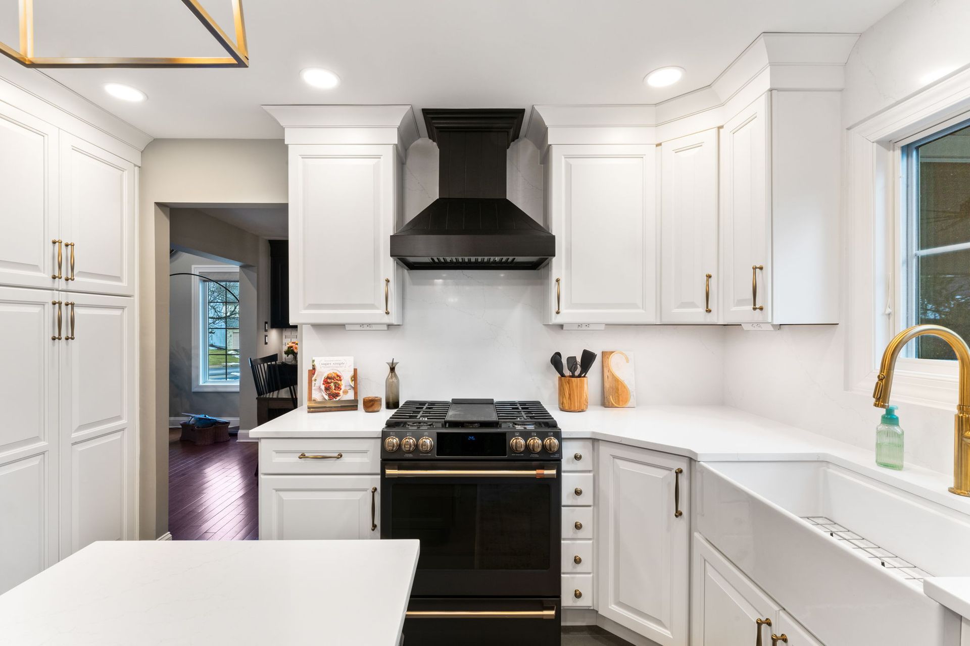 Modern white kitchen with black stove, white cabinets, gold accents, and a large sink near a window In Bucks Country PA