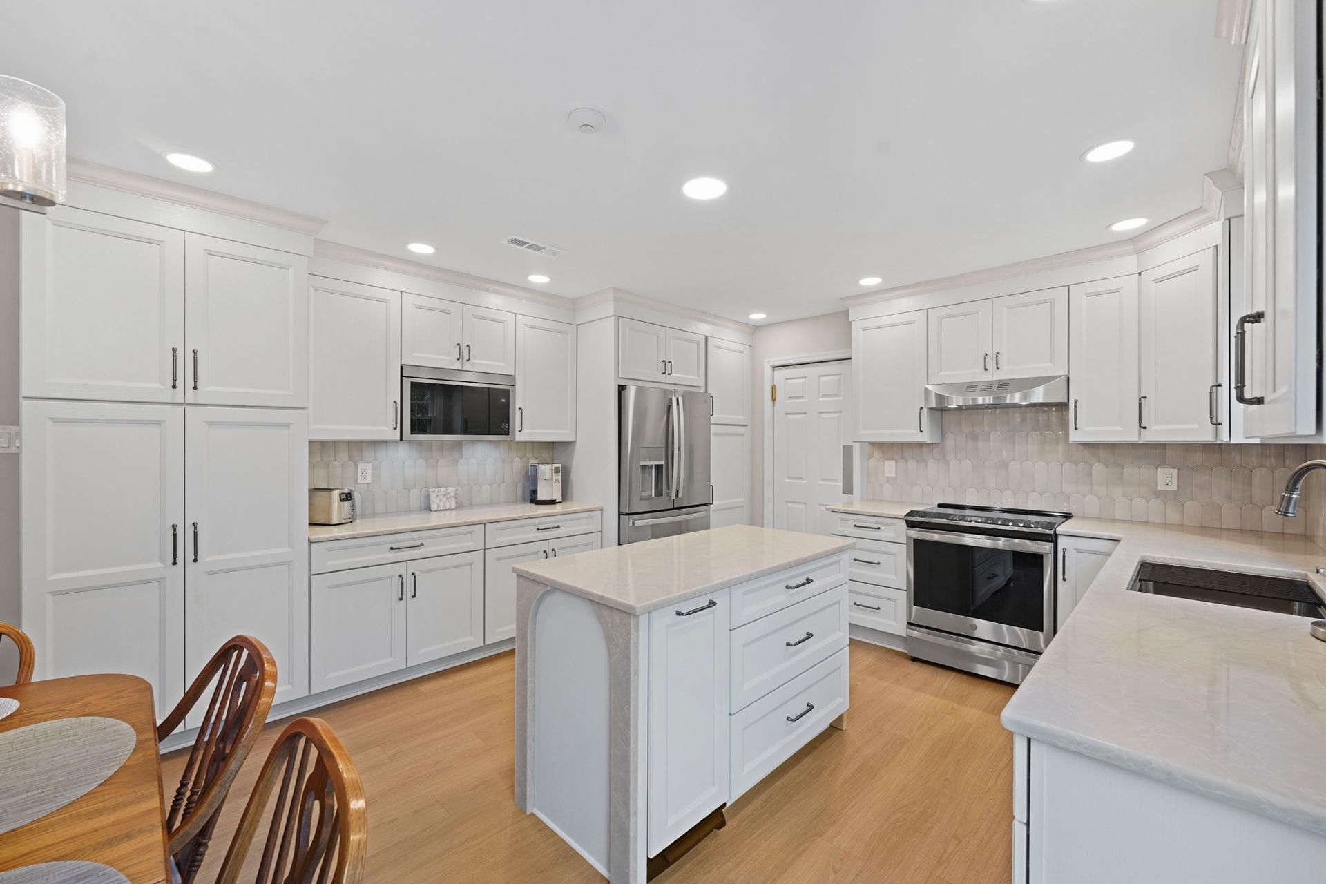 Bright white kitchen with island, stainless steel appliances, light wood floors, and tiled backsplash in Bucks County PA