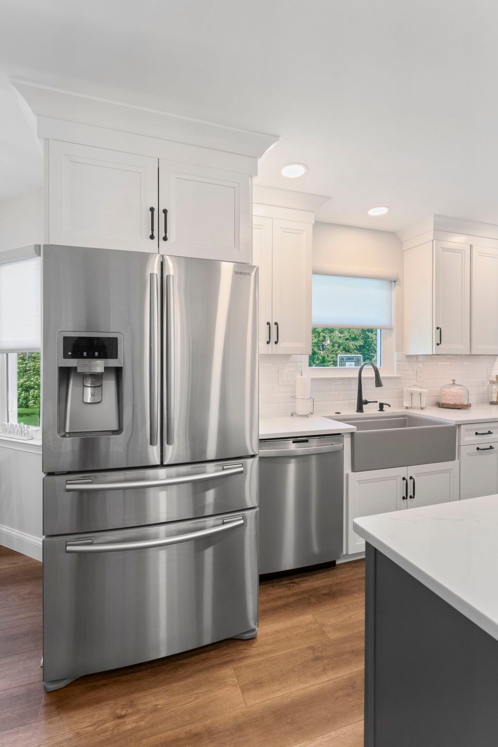Bright white kitchen with stainless steel French-door refrigerator, white cabinets, wood floor, and window over sink In Bucks County PA