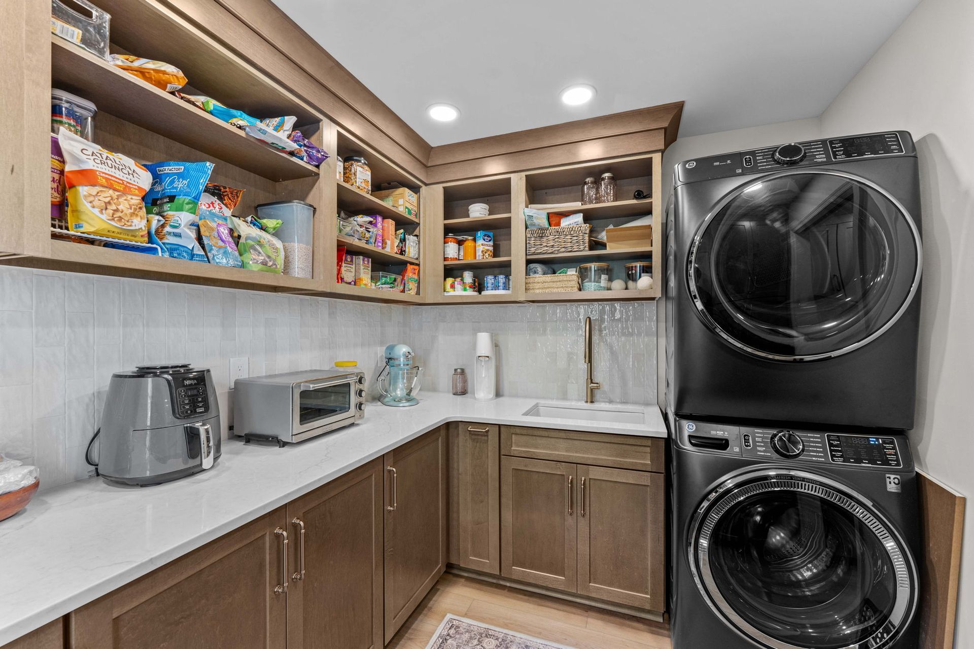 Small pantry-laundry room with white counters, shelves of food, and stacked black washer and dryer in Bucks County PA