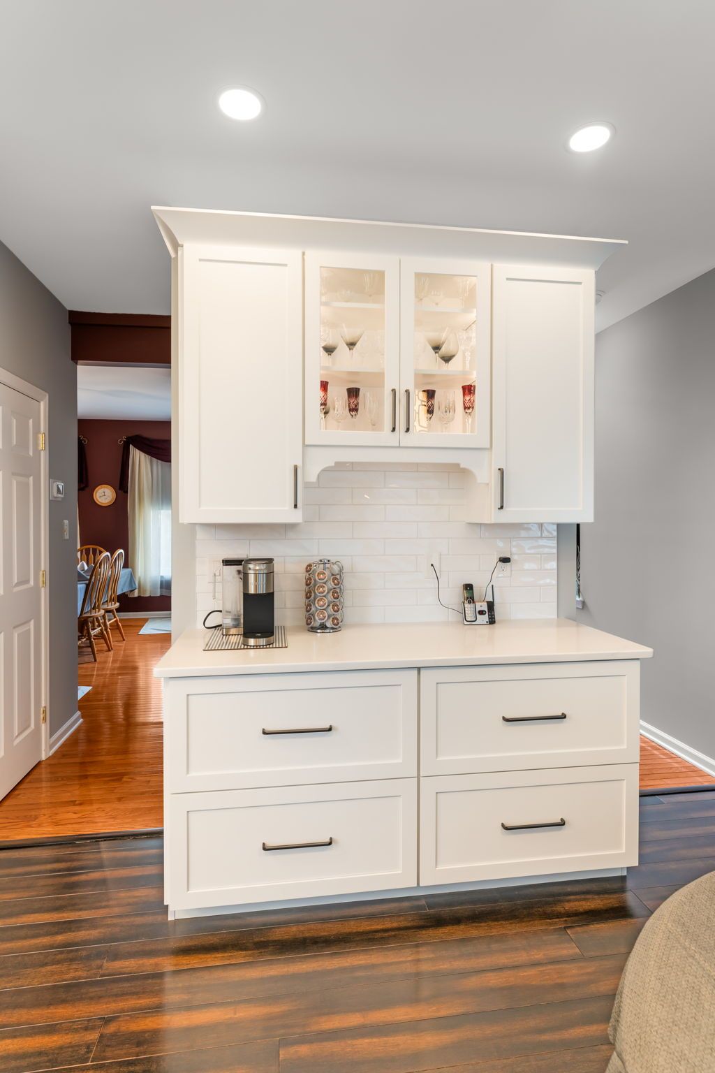White kitchen island cabinet with glass-front upper doors, set in a bright hallway with hardwood floors  In Bucks County PA