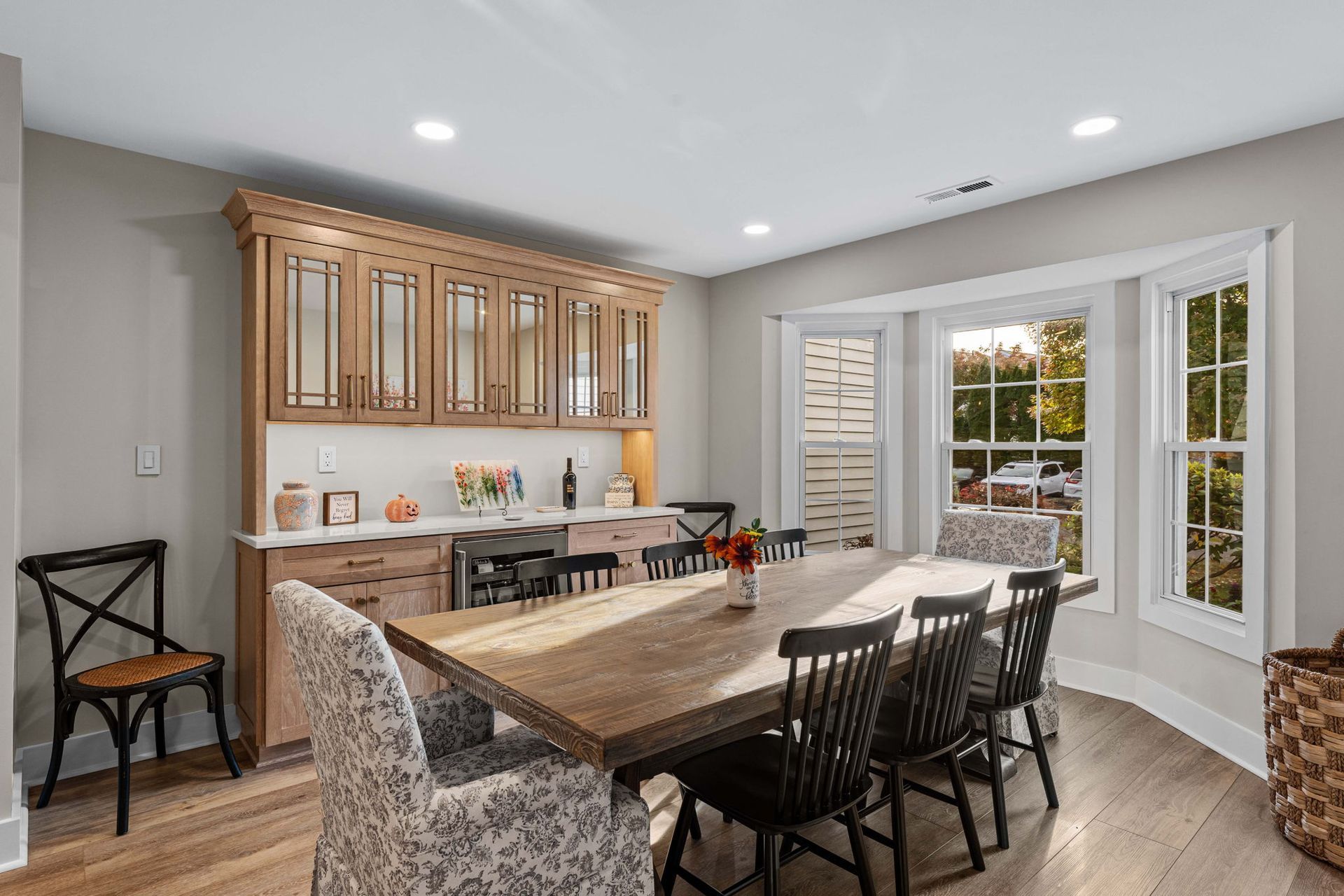 Bright dining room with wooden table, patterned chairs, glass cabinet, and large window seat in Bucks County PA