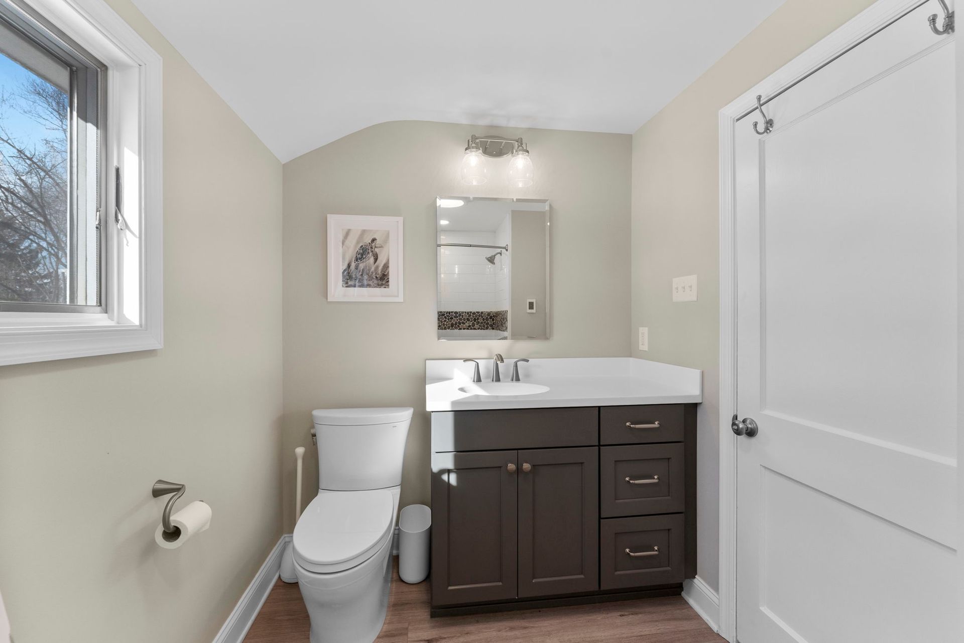 Small bathroom with toilet, vanity sink, mirror, and shower-tub on the right, in beige and dark wood tones  In Bucks County PA