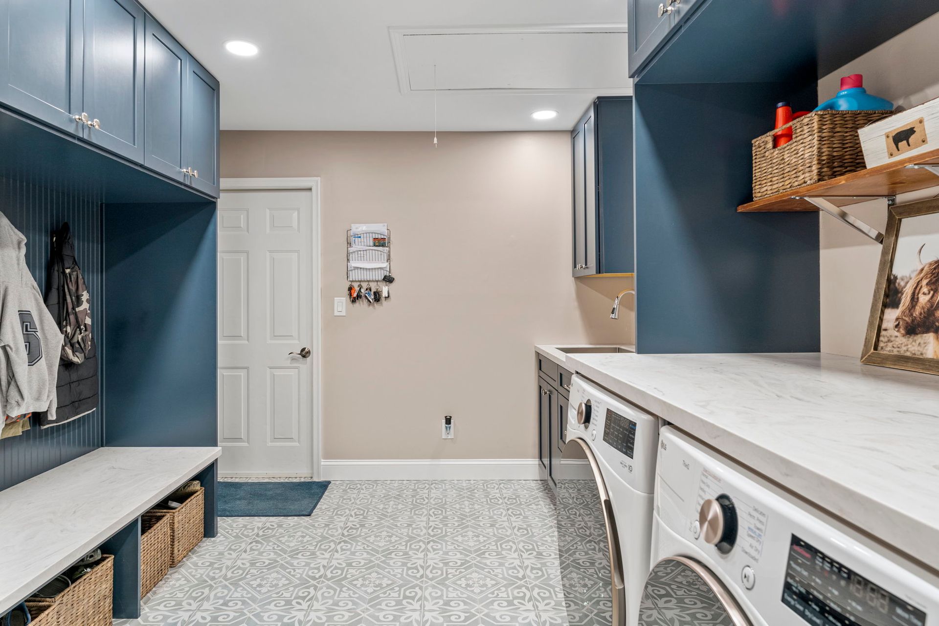 Bright laundry room with blue cabinets, white countertop, washer, dryer, and patterned tile floor In Bucks County PA
