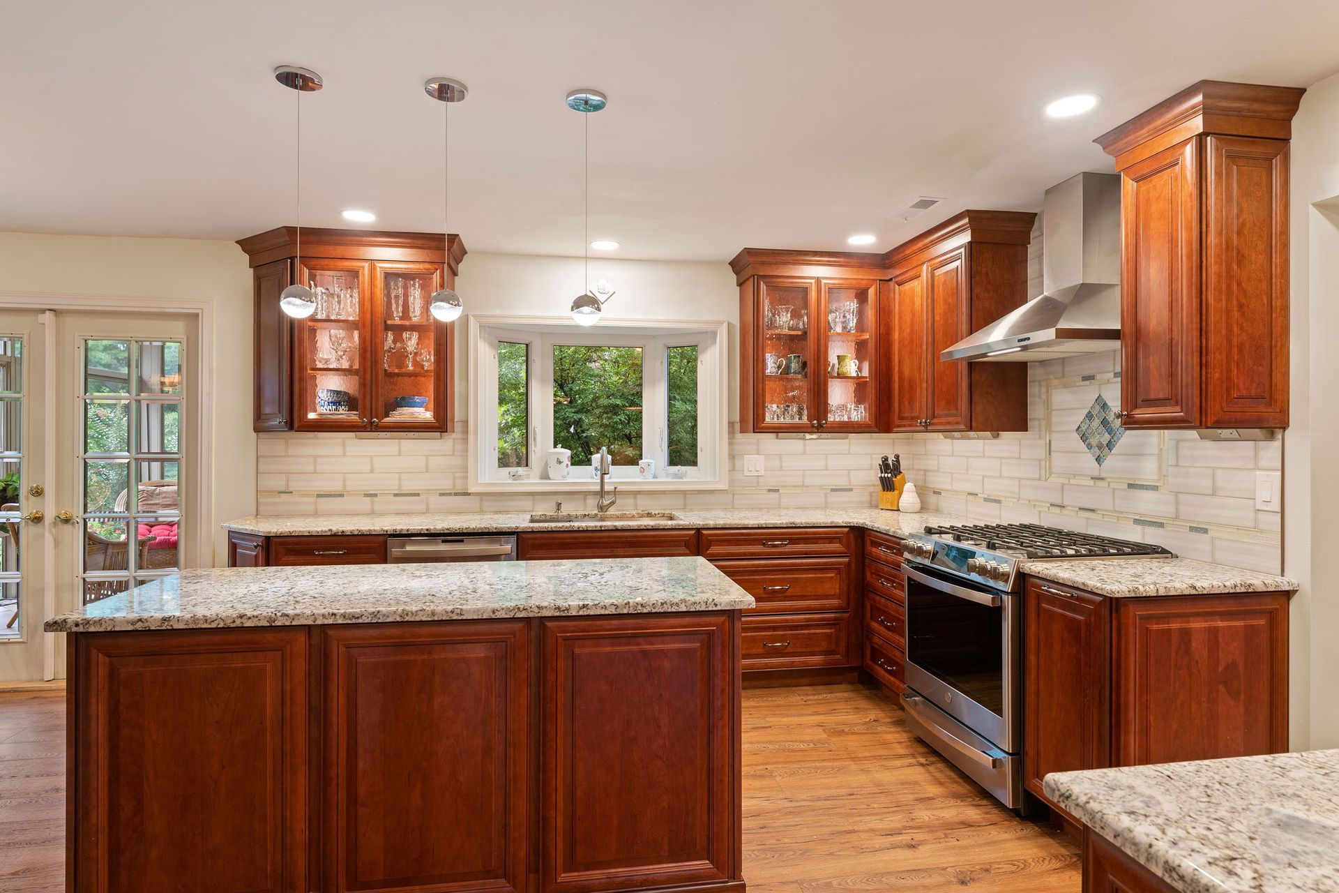 Modern kitchen with cherry wood cabinets, granite counters, island, stainless stove, and two windows  In Bucks County PA