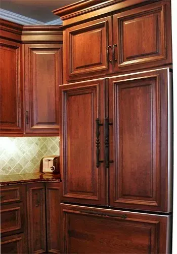 Wooden kitchen cabinets with black handles and a tiled backsplash in warm lighting In Bucks County PA