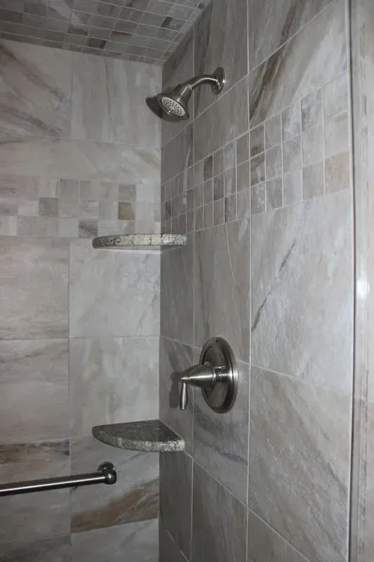 Shower stall with wall-mounted showerhead, grab bar, shelves, and chrome fixtures on beige tile  In Bucks County PA