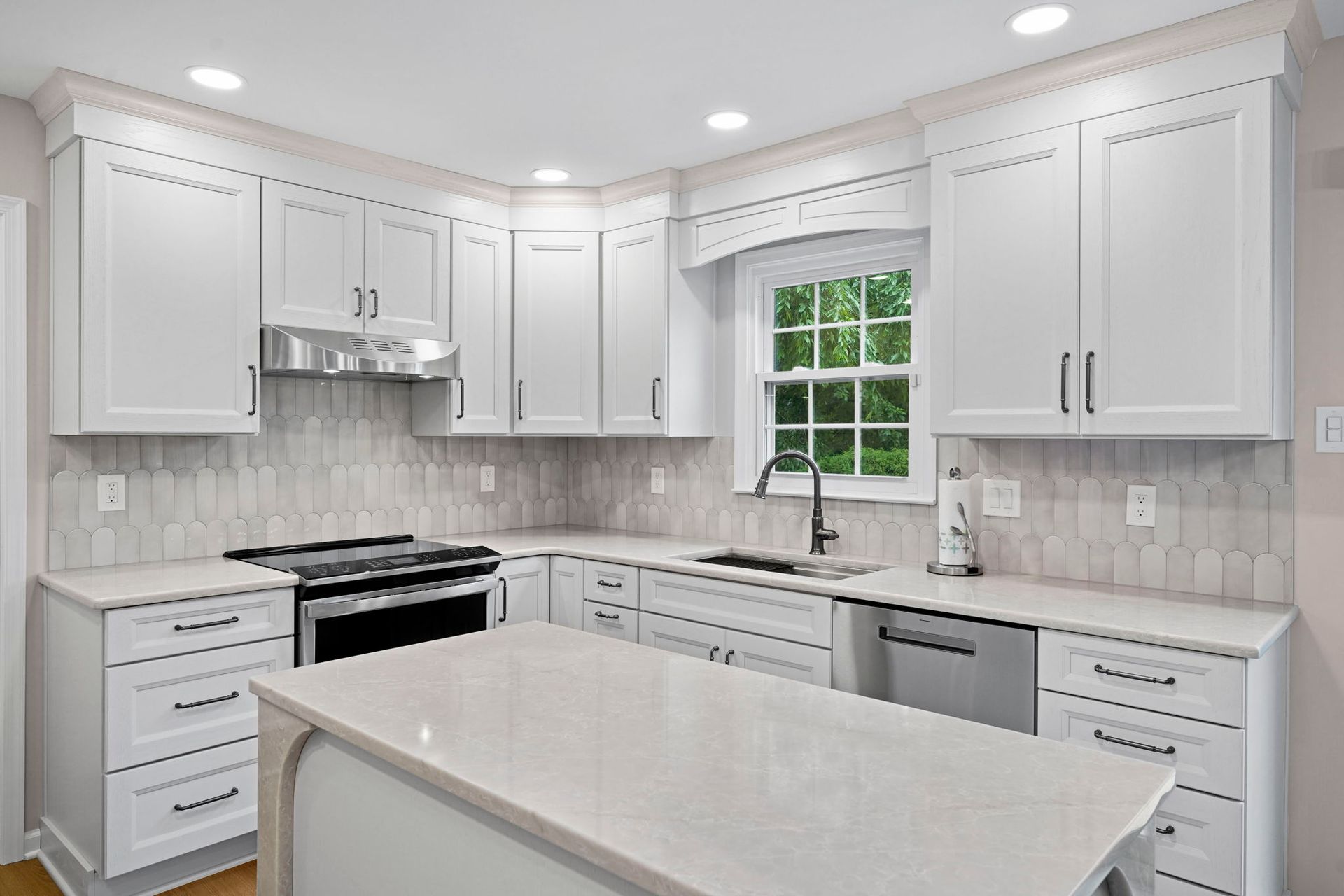 Bright white modern kitchen with island, stove, sink, and tiled backsplash in Bucks County PA