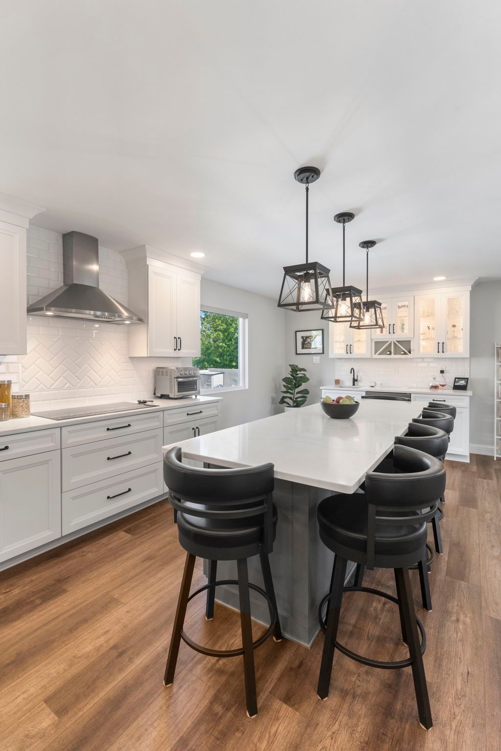 Bright modern kitchen with white cabinets, wood floor, large island, and black bar stools In Bucks County PA