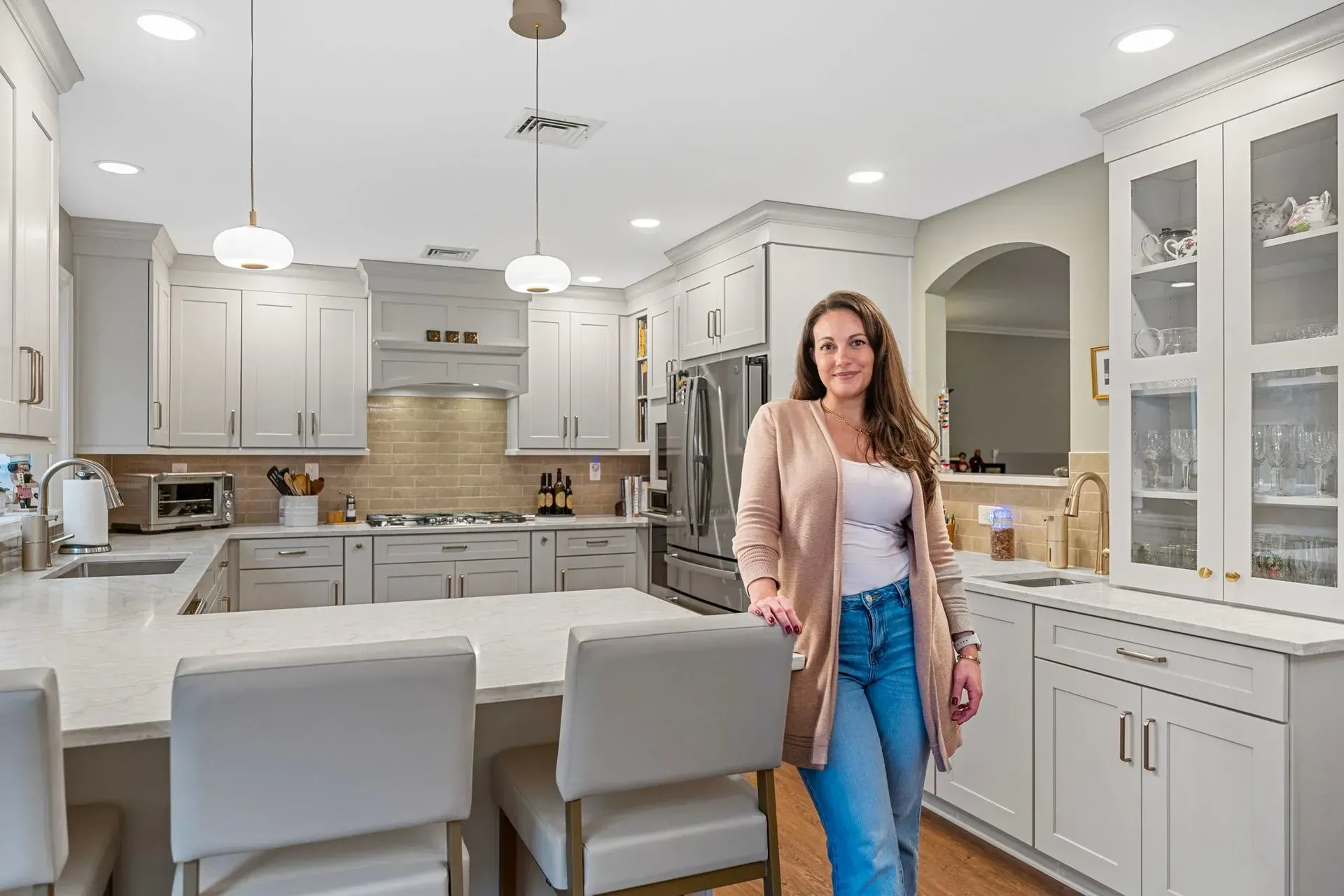 Bright modern kitchen with a woman standing by a white island and cabinets, smiling toward the camera In Bucks County PA