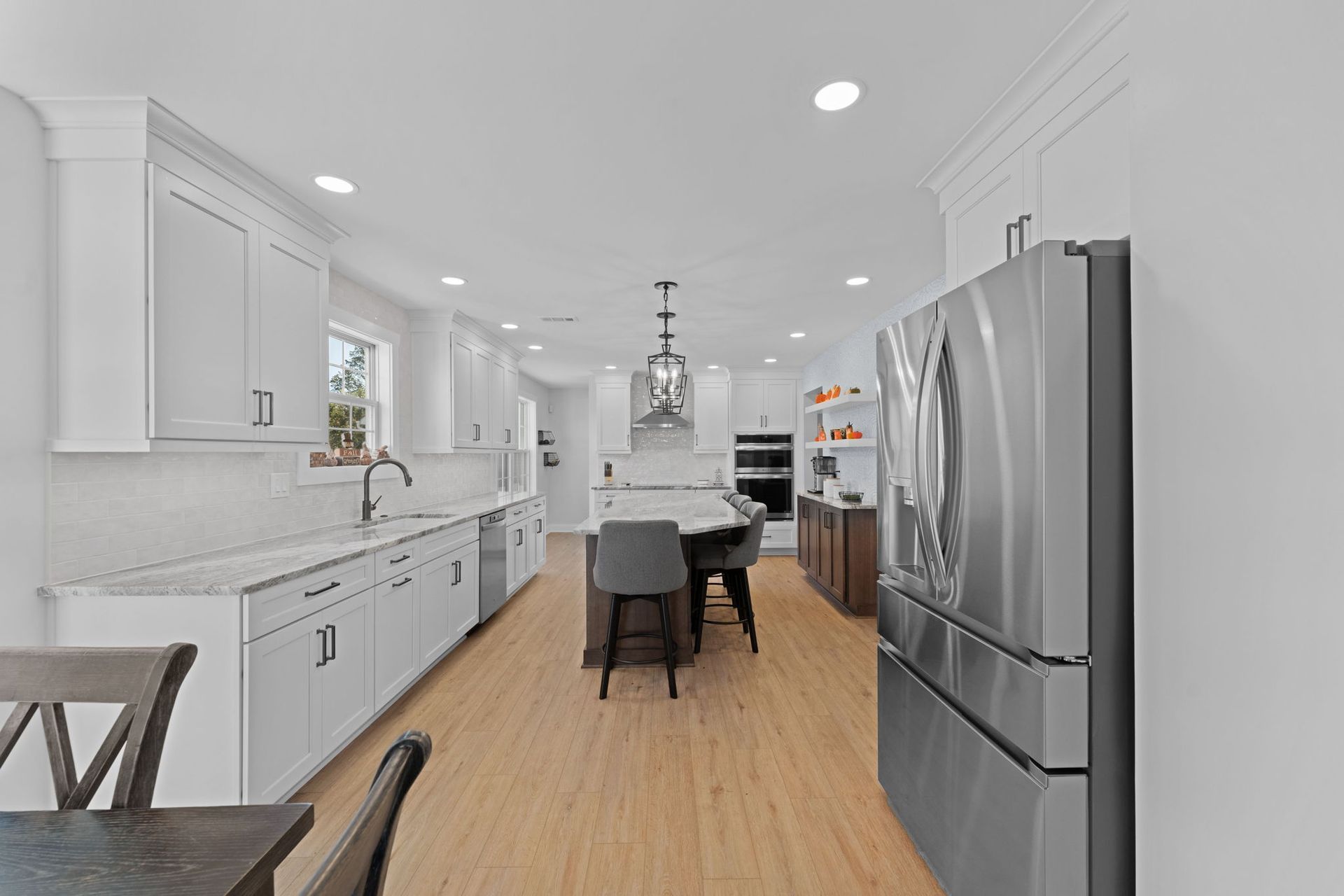 Bright white modern kitchen with stainless steel appliances, wood floor, island seating, and pendant lights  In Bucks County PA