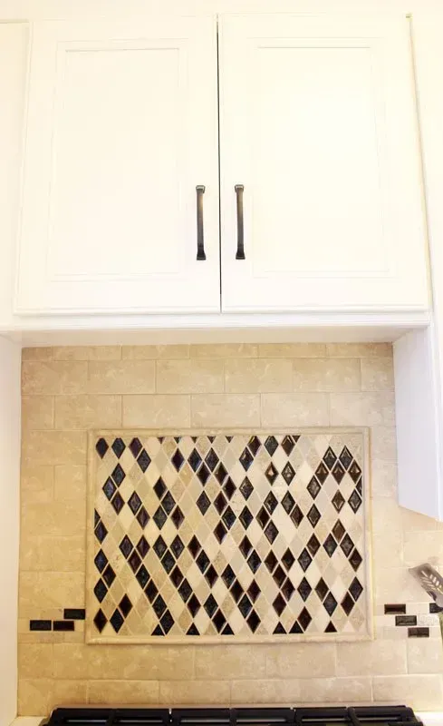 White kitchen cabinets above a tiled backsplash with a black-and-tan diamond mosaic pattern In Bucks County PA