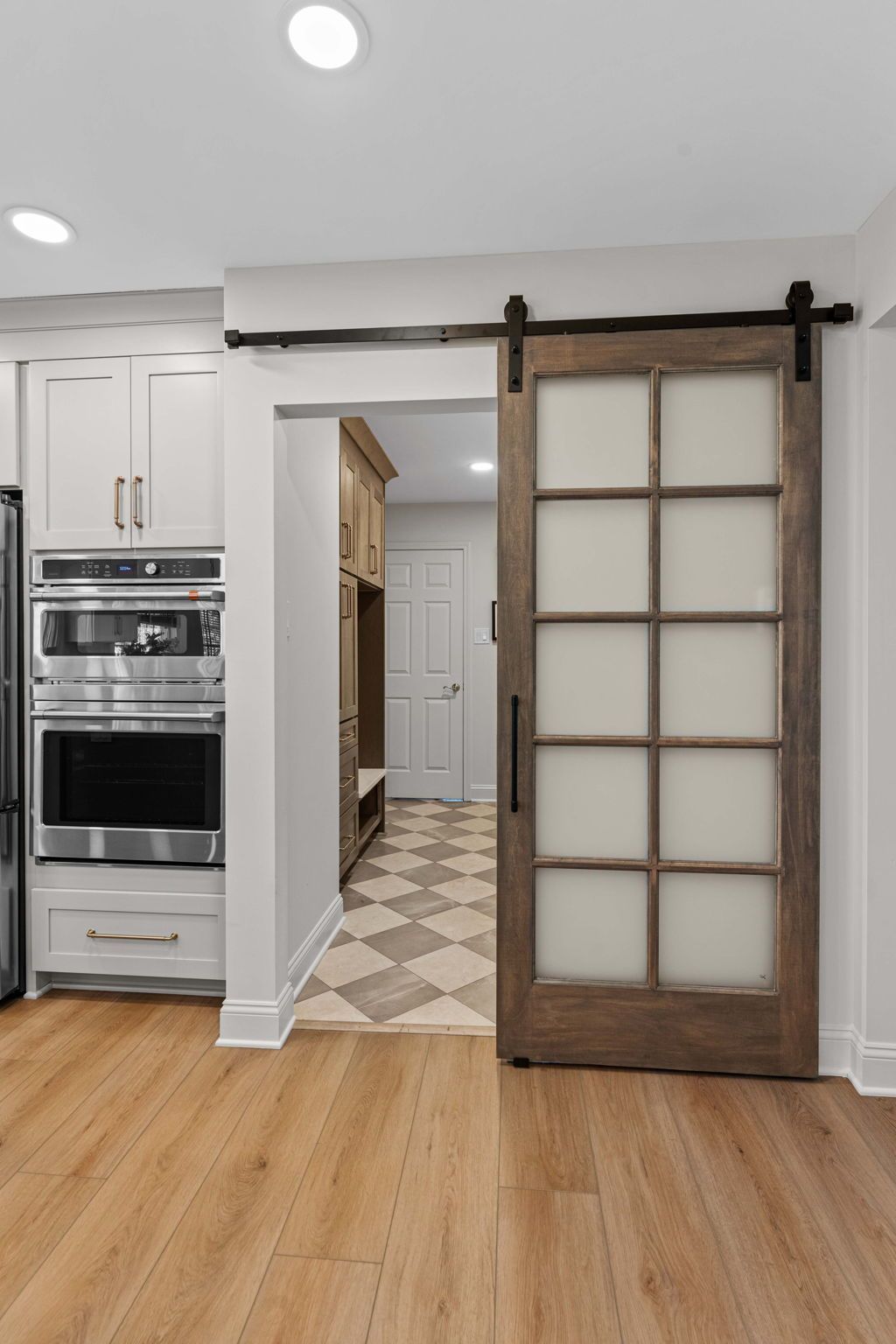 Kitchen with wood floor and a rustic sliding barn door opening to a hall with patterned tile flooring in Bucks County PA