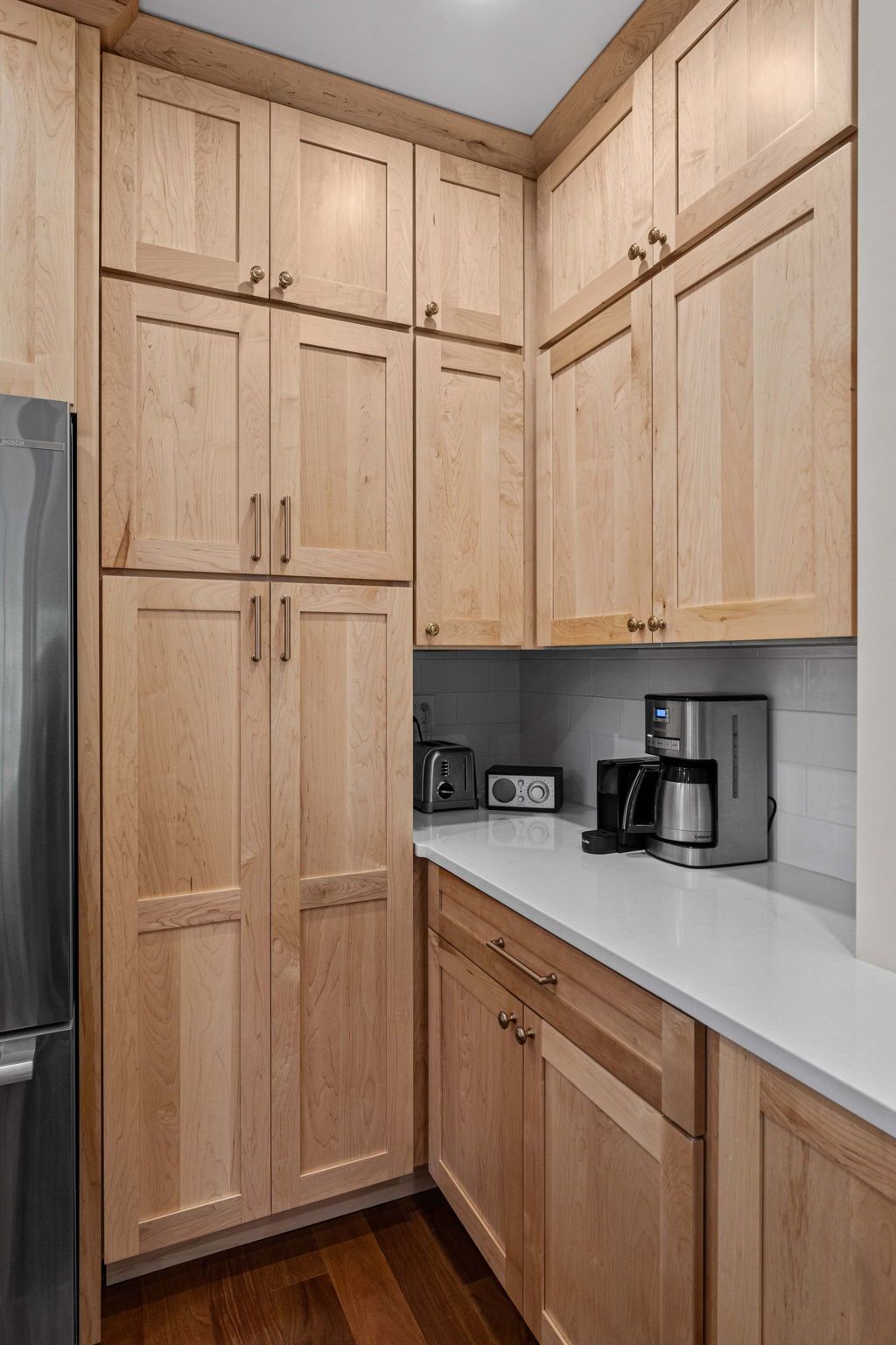 Tall wood kitchen cabinets in a corner kitchen with white countertops and a coffee maker In Bucks County PA