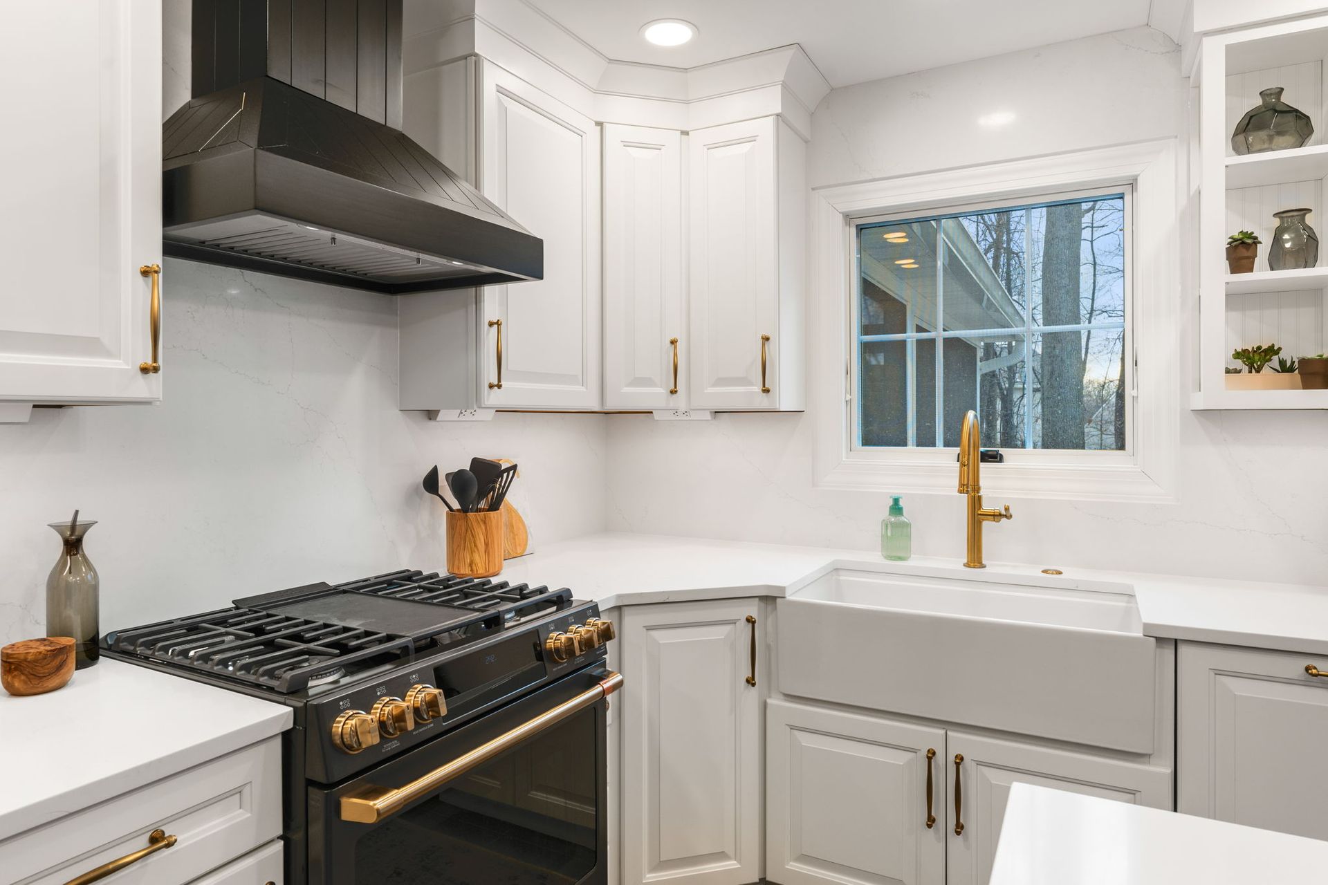 Bright modern kitchen with white cabinets, black stove, farmhouse sink, and brass faucet In Bucks Country PA