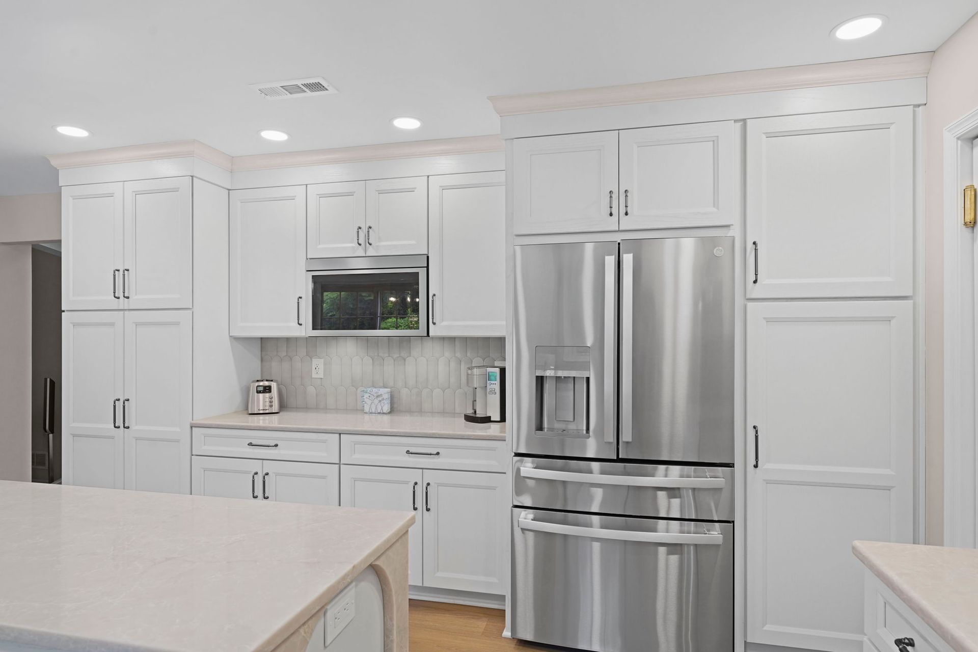 Bright white kitchen with stainless steel refrigerator, microwave, and cabinets, seen from an island countertop in Bucks County PA