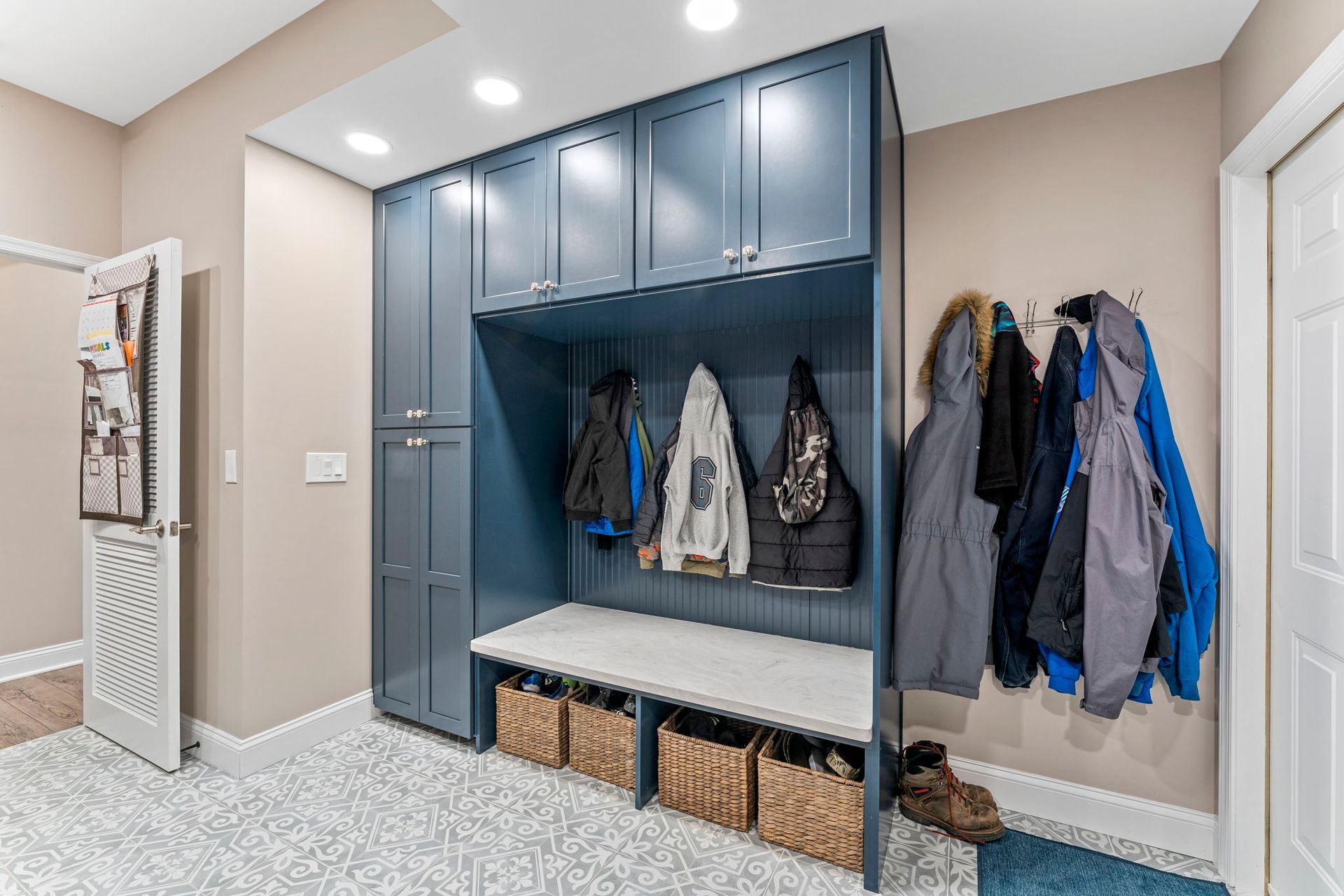 Built-in blue mudroom cabinets with bench, hooks, and hanging coats in a bright entryway In Bucks County PA