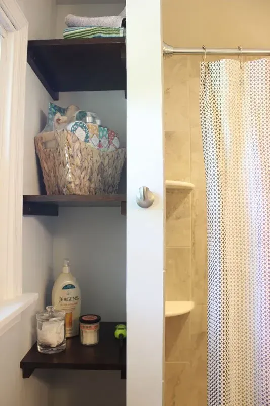 Bathroom shower stall with beige curtain and dark wood shelves holding towels and toiletries  In Bucks County PA