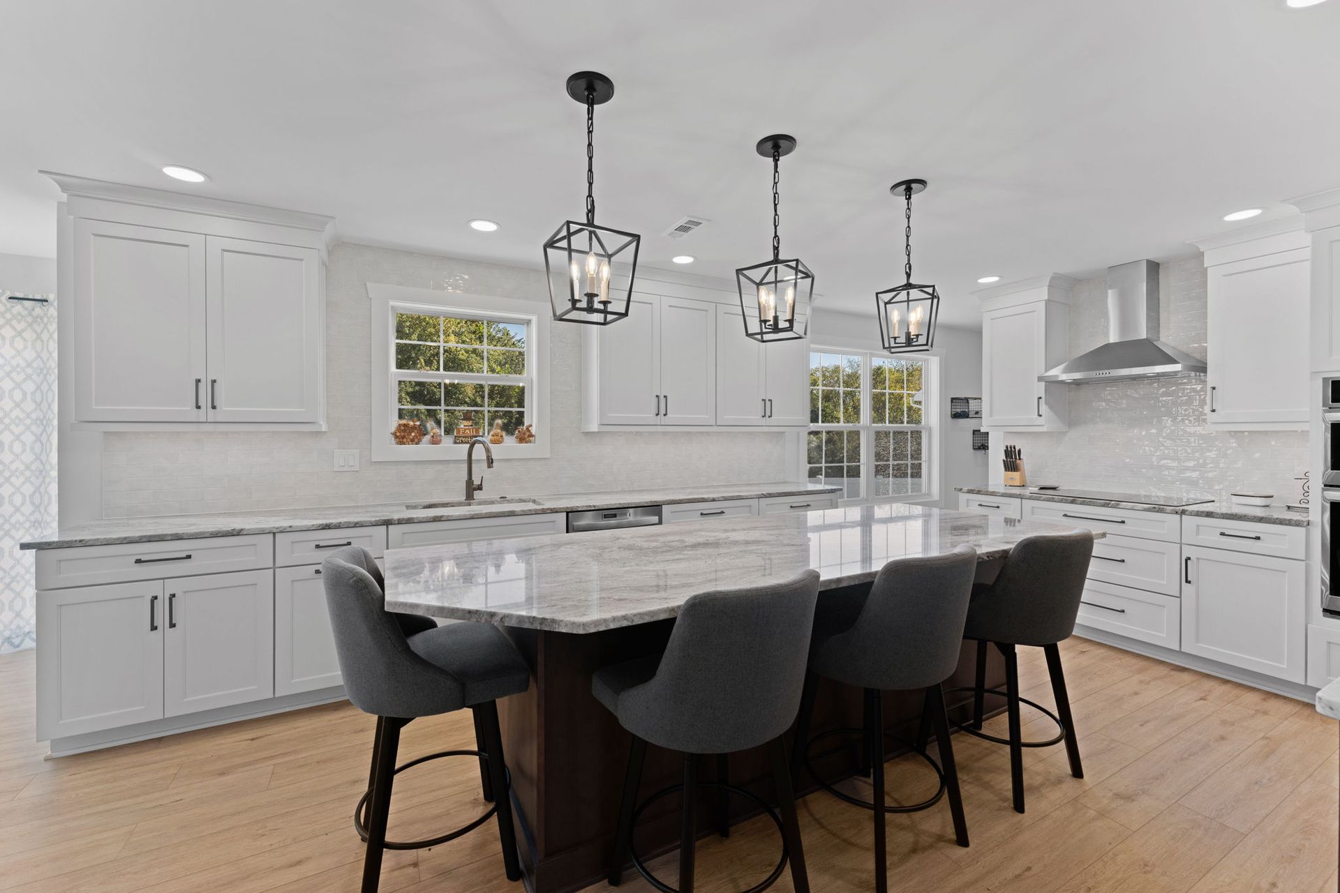 Bright modern kitchen with white cabinets, marble island, dark barstools, and pendant lights  In Bucks County PA