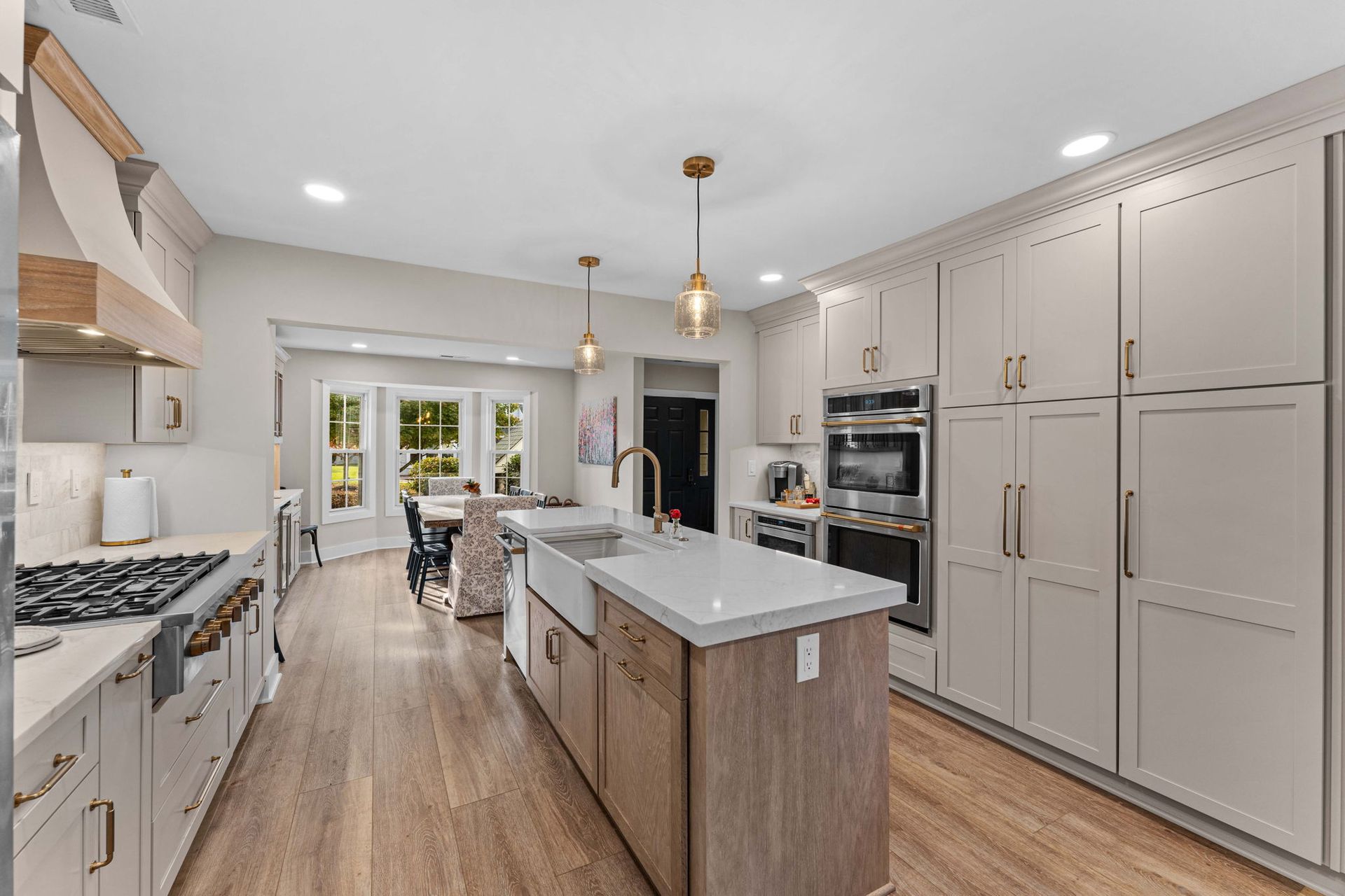 Bright modern kitchen with white cabinets, gray island, wood floors, and dining area beyond in Bucks County PA