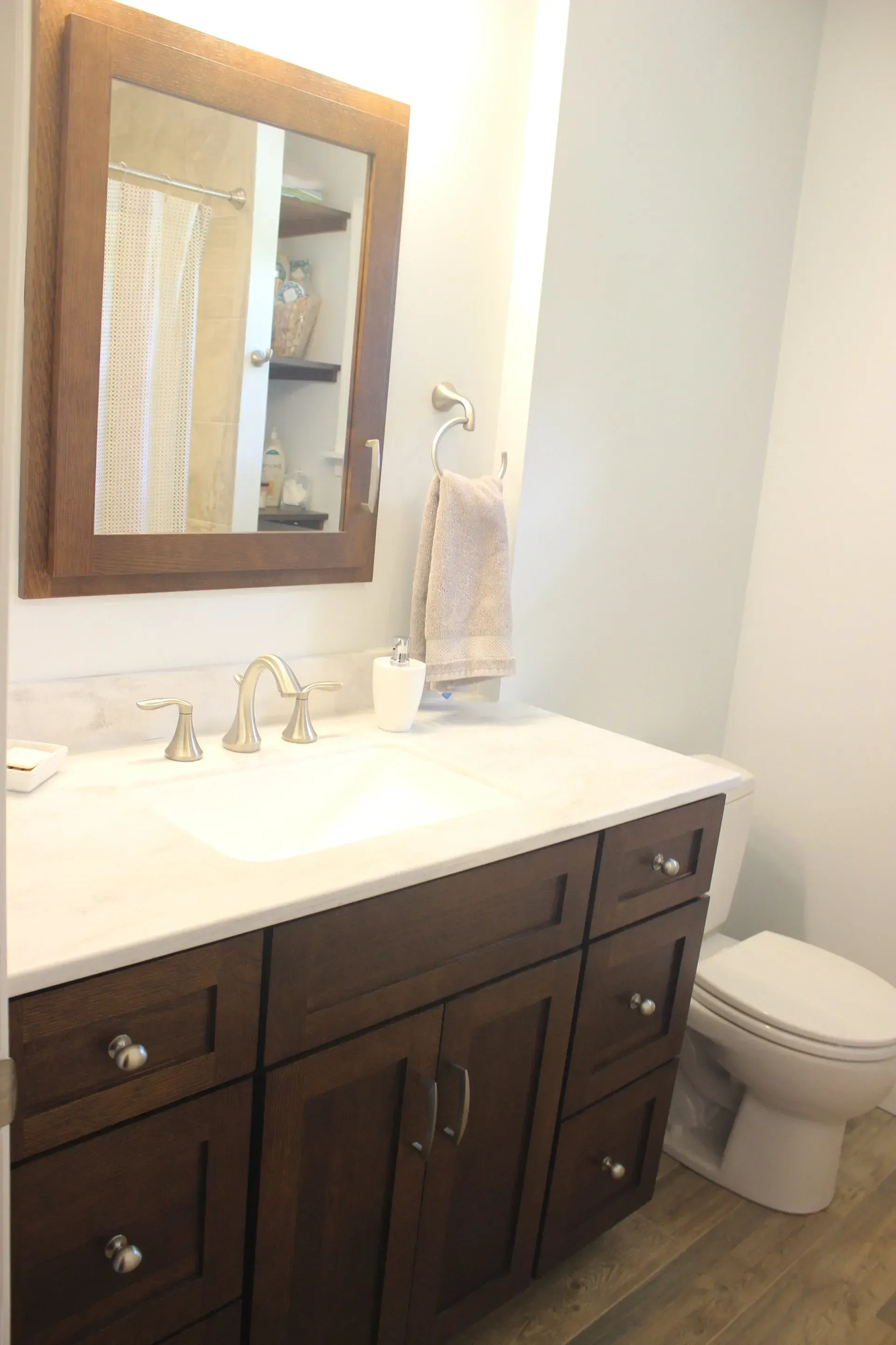 Bathroom vanity with dark wood cabinets, white countertop, mirror, sink, and toilet beside it In Bucks County PA